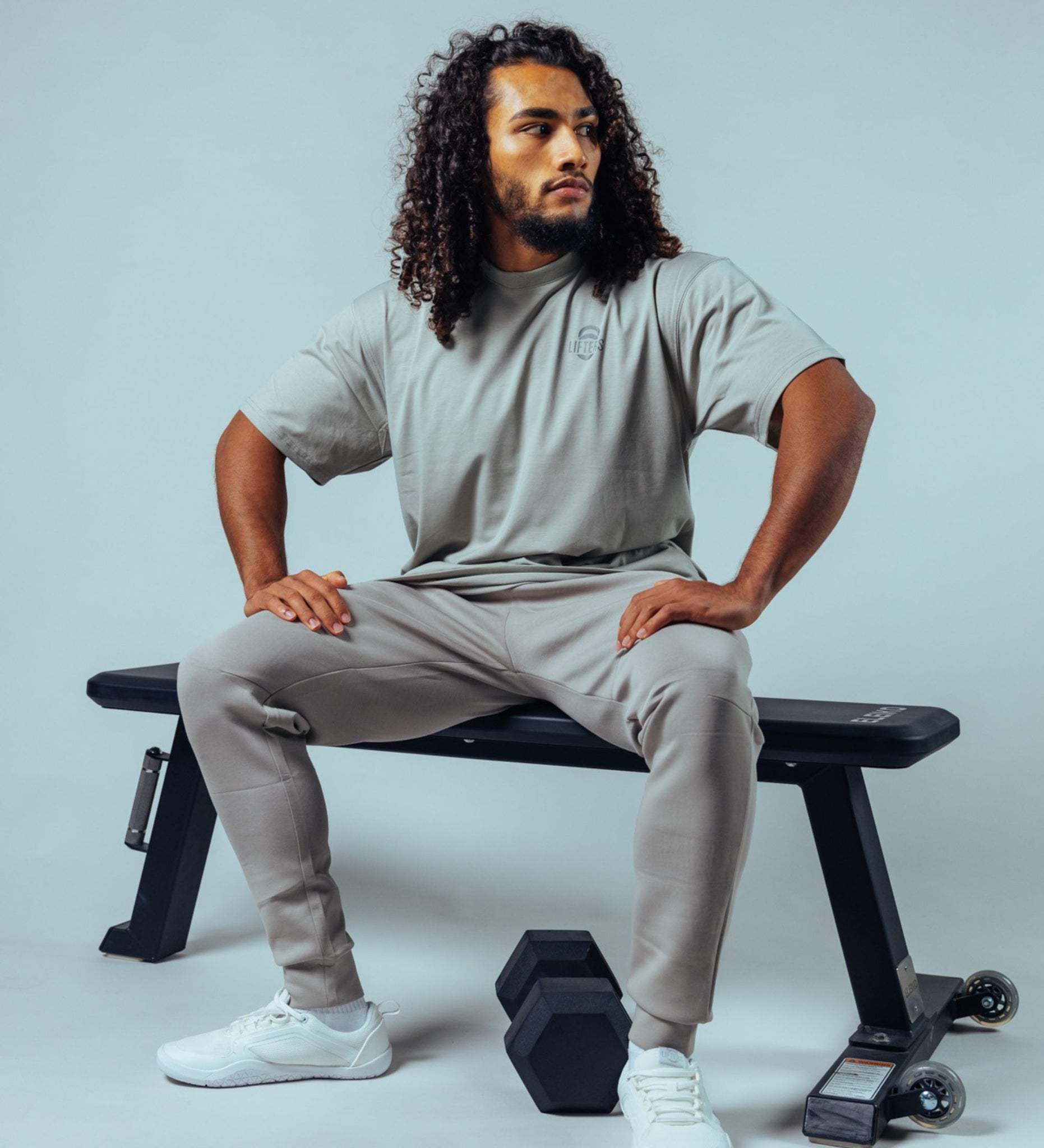 Mann sitzend auf Trainingsbank in Gym Kleidung von Lifters Wear, mit T-Shirt, Jogginghose und Barfußtrainingsschuhen, bereit für das Fitness-Training.