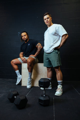 Two men wearing Lifters Gym Wear shirts and athletic shorts are ready for strength training.