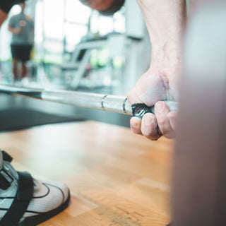 Athlet hat das Lifters Hook Grip Tape um seinen Daumen gewickelt und greift die Langhantel